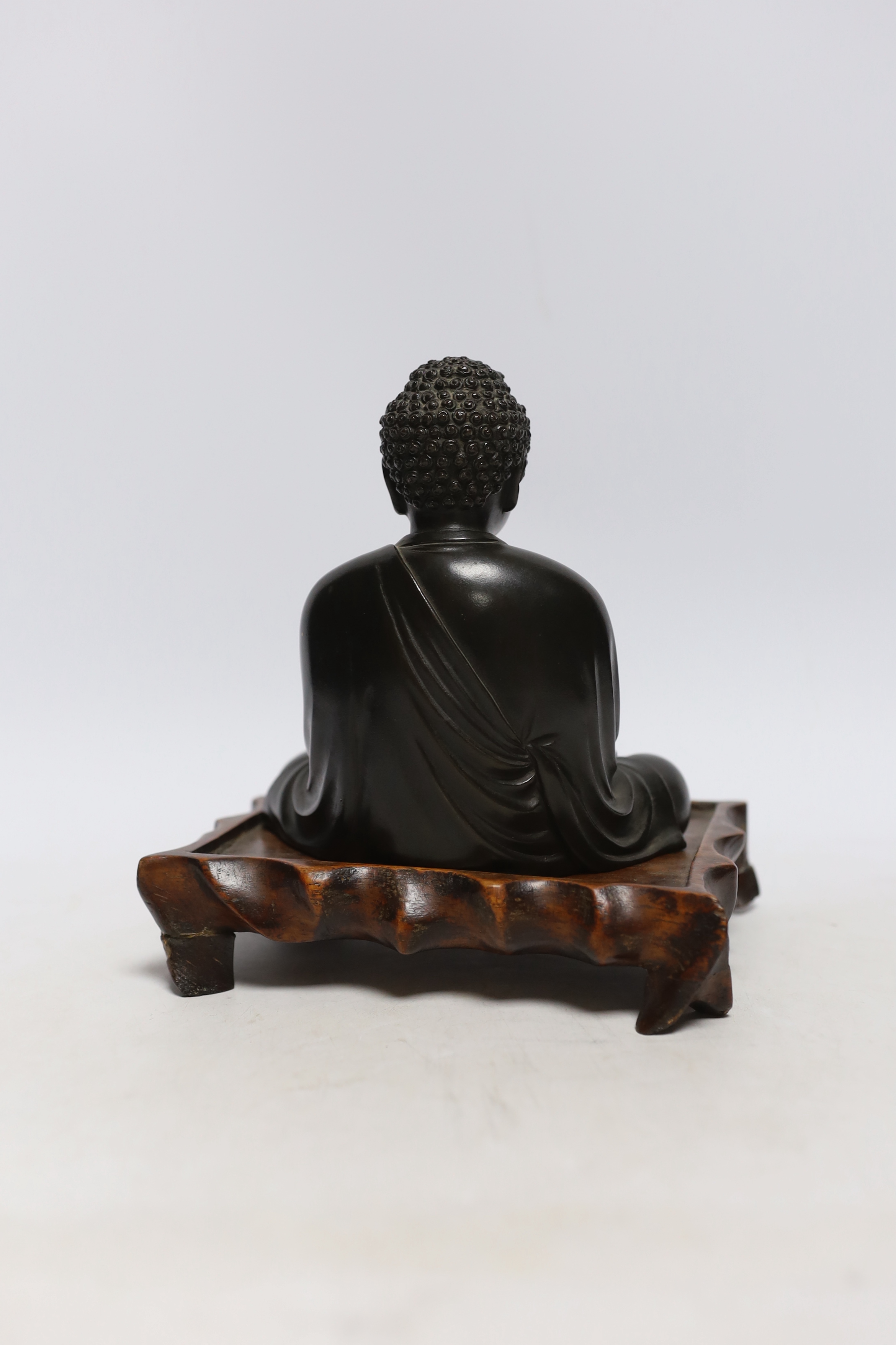 A Japanese bronze figure of Buddha, Meiji period, inscribed seven character mark to base, on a hardwood stand, 15cm high